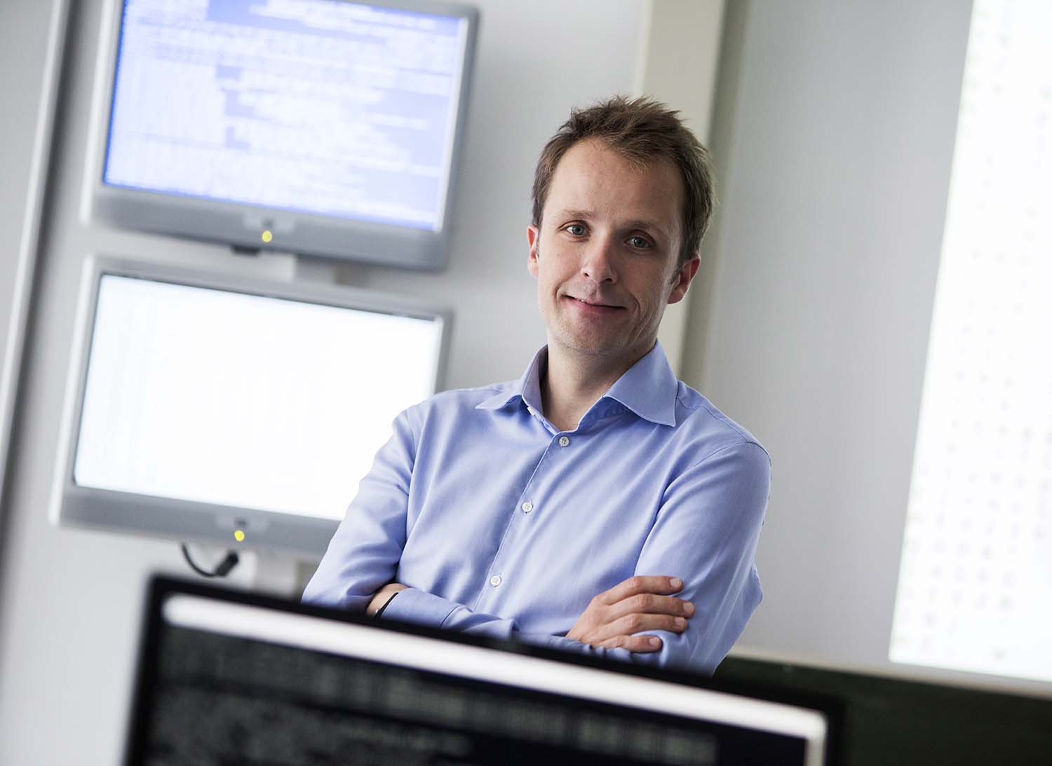 Das Foto zeigt eine Person mit verschränkten Armen und einem blauen Hemd, im Hintergrund zwei Bildschirme Prof. Dr. Sebastian Schinzel von der FH Münster | Foto: Wilfried Gerharz