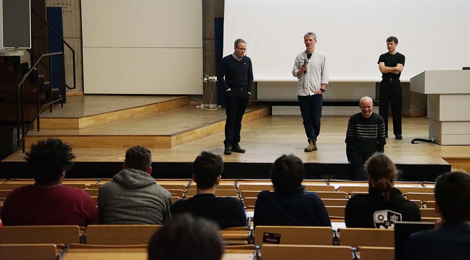 Vier Redner stehen vorne im Hörsaal Audimax der TU Berlin, dahinter eine Leinwand. Vorne sind Zuhörende von hinten in den Stuhlreihen zu erkennen. Foto: Iven Jurk | DFN